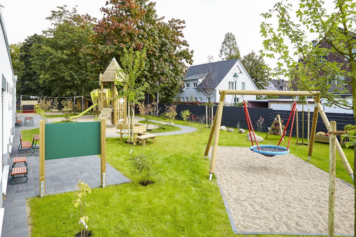 Playground equipment for childcare facilities from eibe - playground equipment with play tower, nest swing over a sandy surface and various seats.