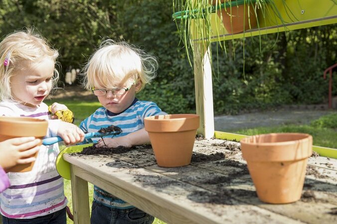 Playground equipment for childcare facilities from eibe - two children planting flower pots on a wooden bench.