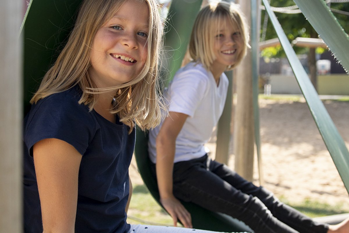 School playground planning - two smiling girls sitting on eibe playground equipment in their School playground. 
