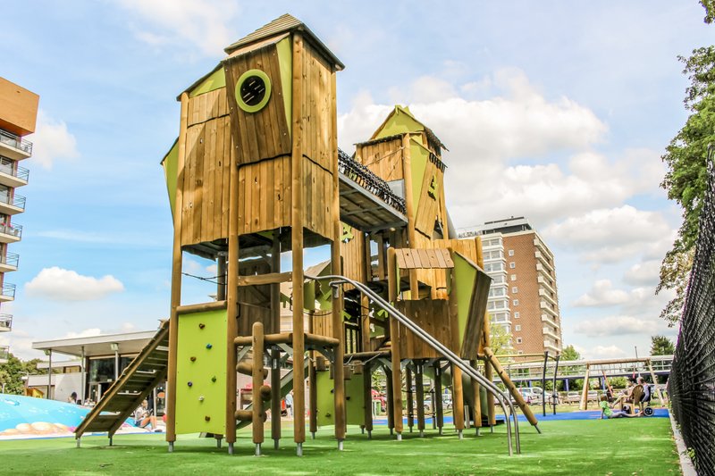 Public playgrounds - eibe play equipment on a well-kept green space in front of an urban backdrop. 